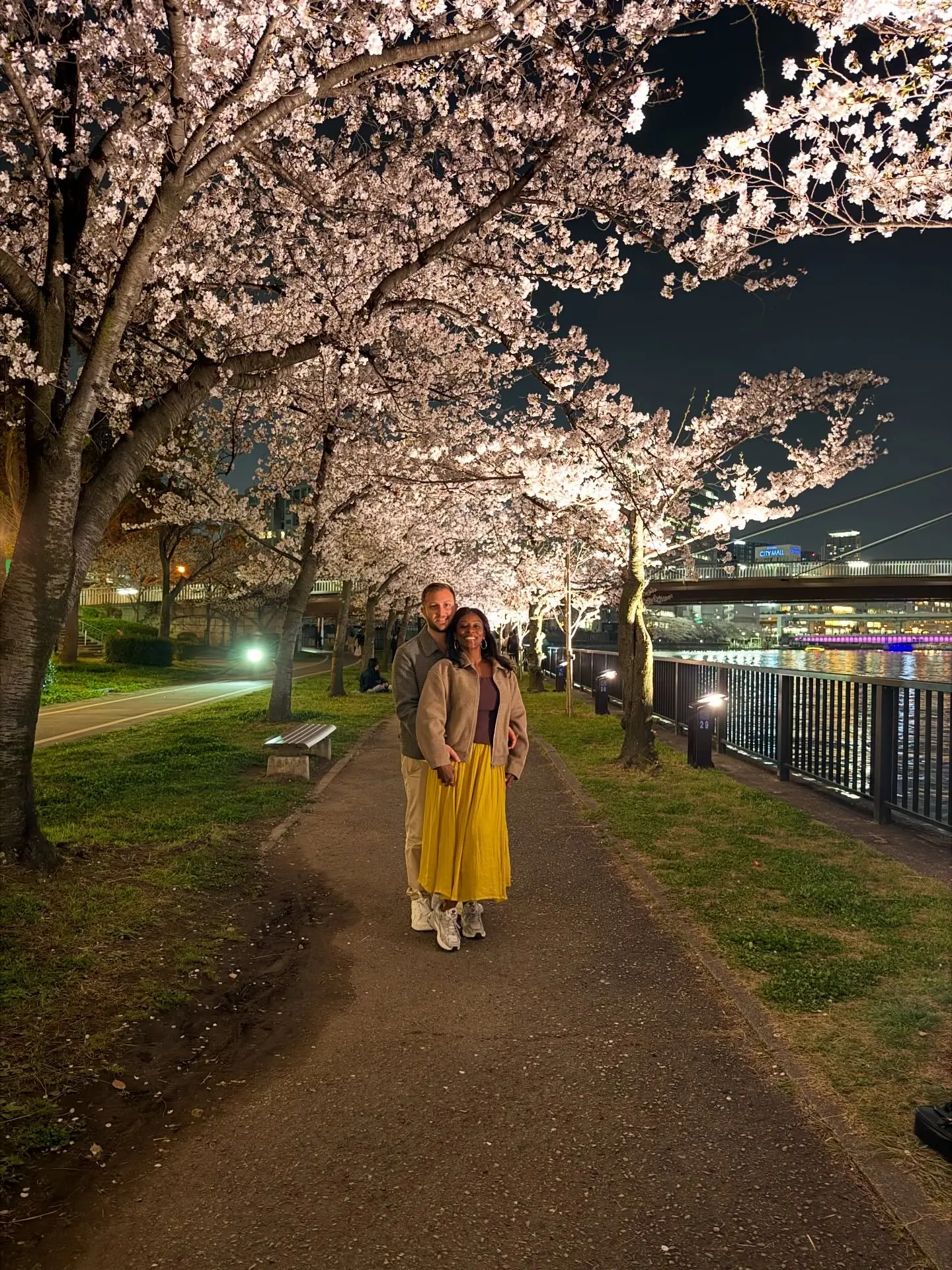 Us under a tunnel of illuminated cherry blossom by the river at night