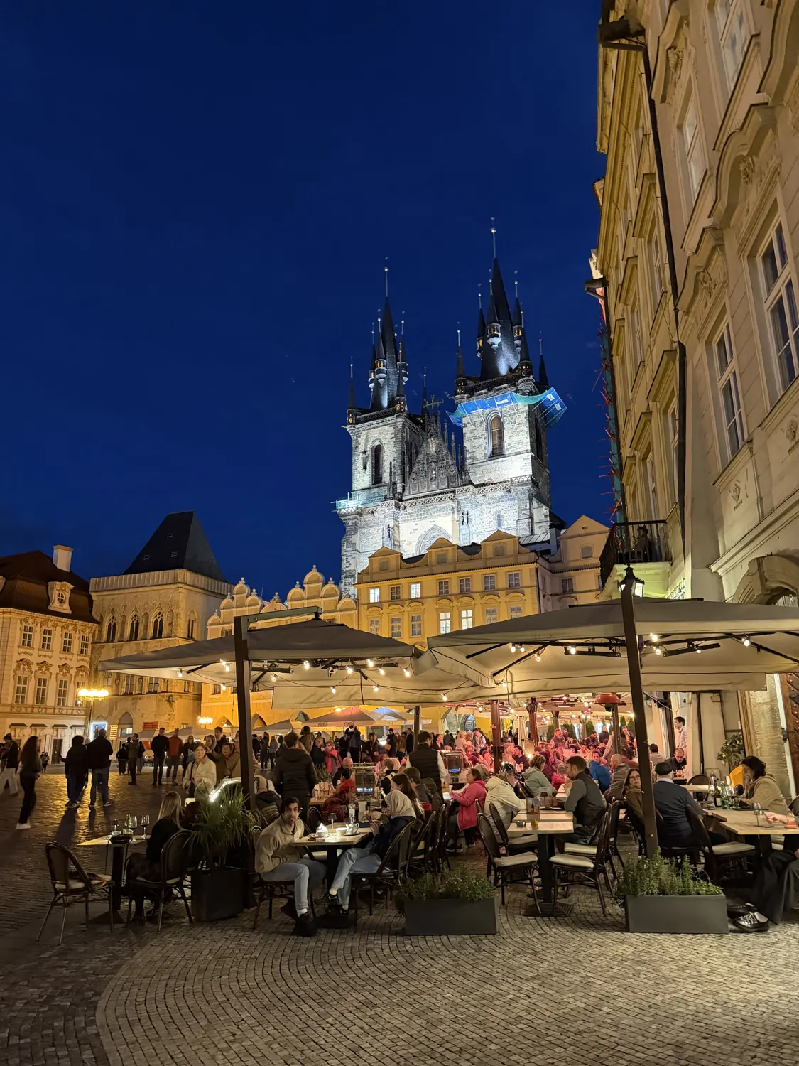 Old Town Square at night with the glowing spires of the Týn Church above the restaurants