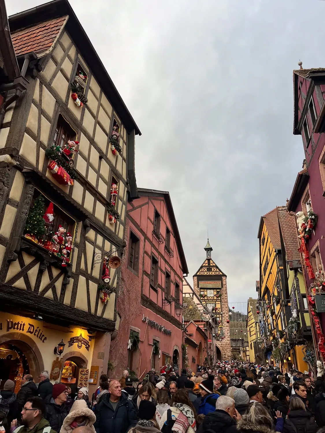 The crowded festive main street of Riquewihr, decorated timber houses leading up to the Dolder tower