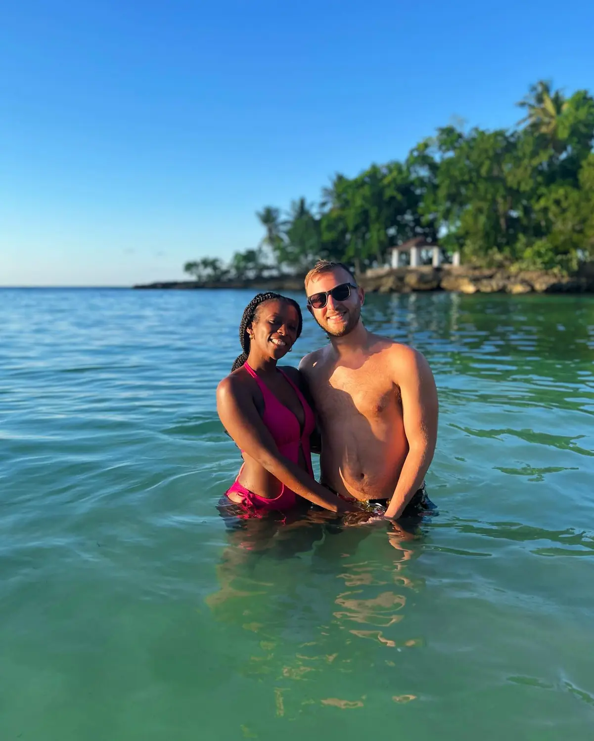Us in calm golden-hour water beside a gazebo on a rocky point in Samaná