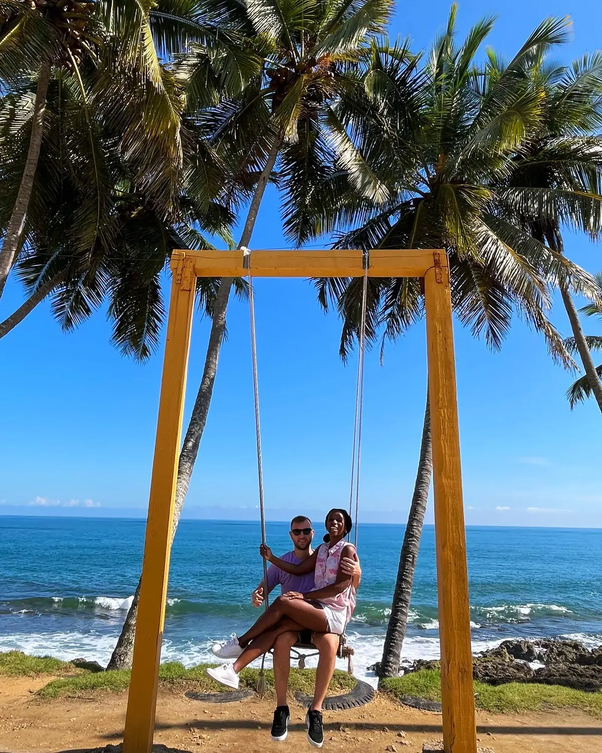 Us on a big yellow swing under palm trees above the rocky ocean coast in Samaná