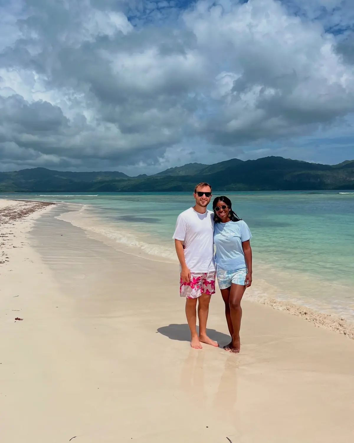 Us on a sandbar with green mountains rising across calm turquoise water in Samaná