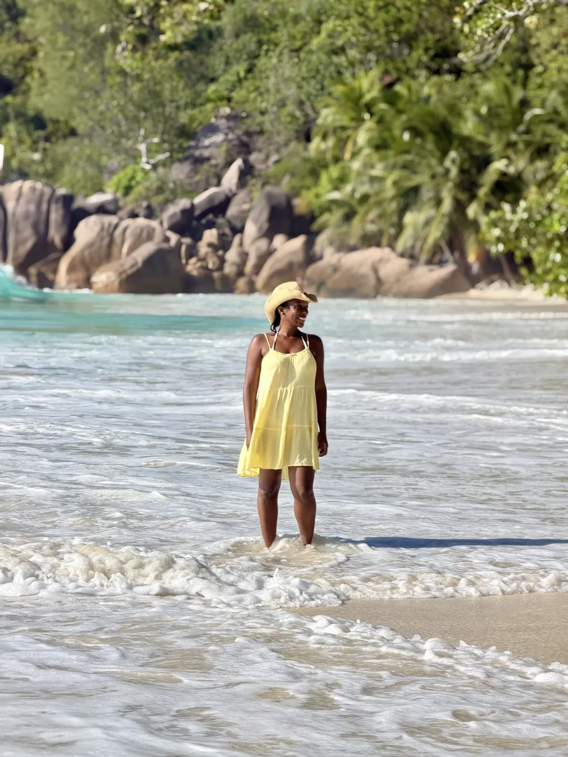 Melody in a yellow sundress standing in the surf at Anse Lazio, Praslin