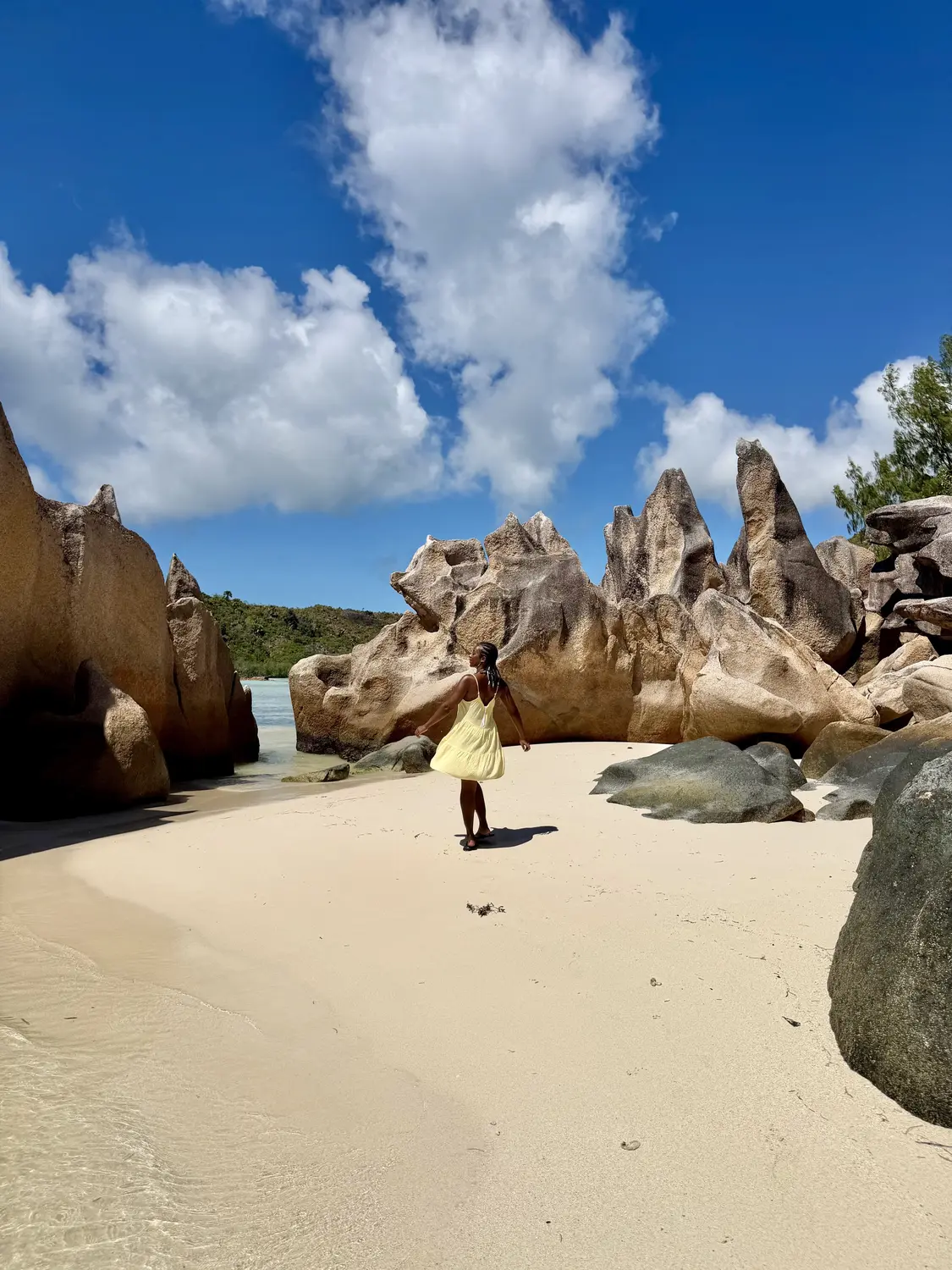 Melody twirling in a yellow dress on a white-sand cove surrounded by jagged granite on Curieuse Island