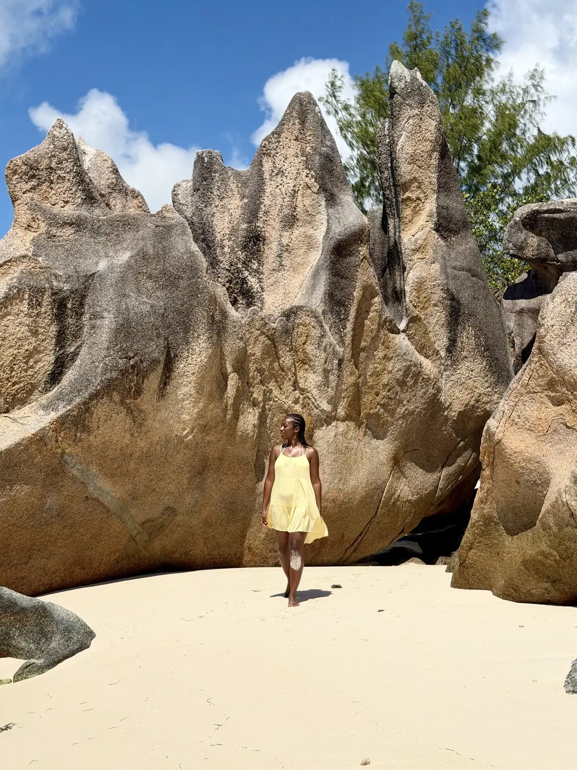 Melody walking in front of towering granite spires on a Curieuse beach