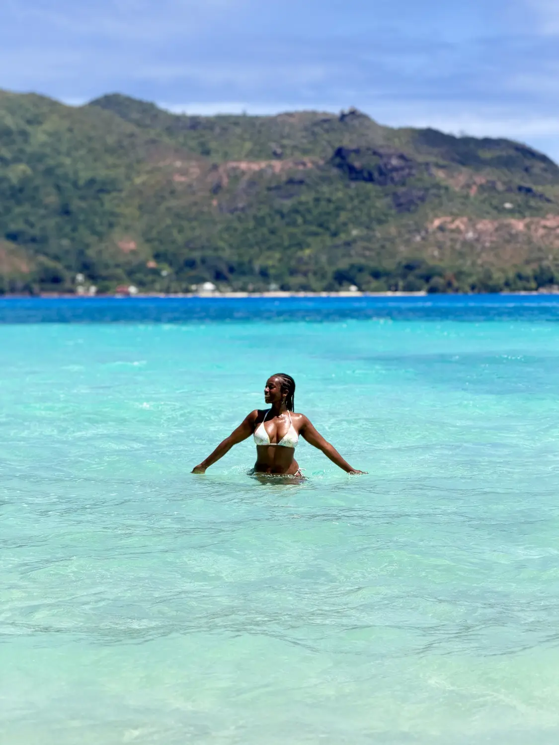 Melody swimming in bright turquoise water off Curieuse with Praslin's hills behind