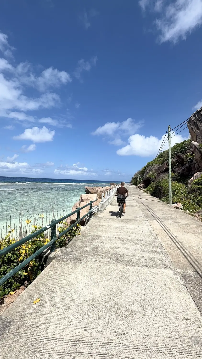 Andrew cycling along La Digue's seaside road beside the reef
