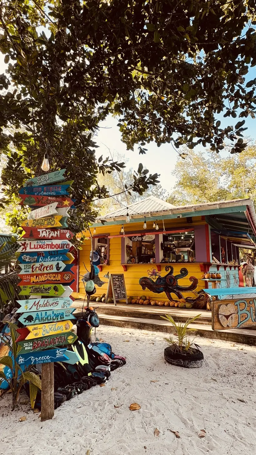 A colourful beach café with a painted octopus mural and a signpost of hand-painted country arrows on La Digue