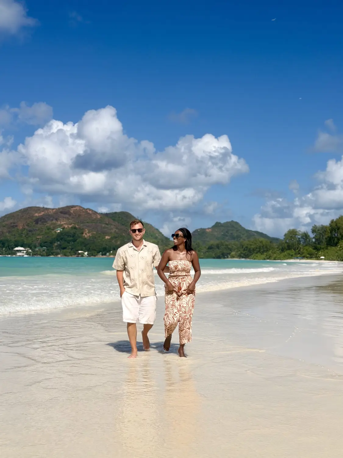 Us walking along the powder-white shoreline of Côte d'Or with turquoise water and green hills behind, Praslin