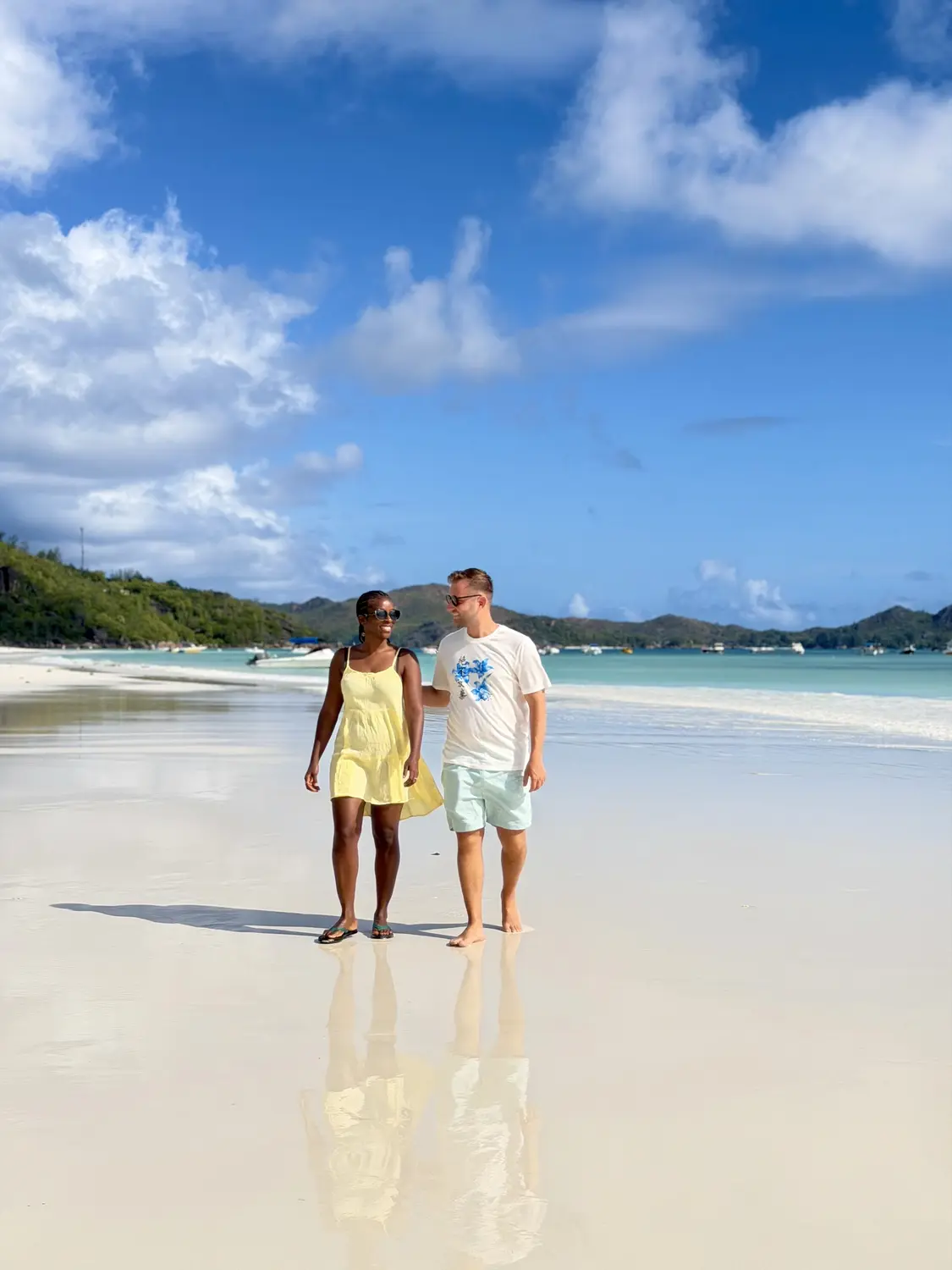 Us strolling on the glassy wet sand of Côte d'Or beach with boats moored in the bay, Praslin