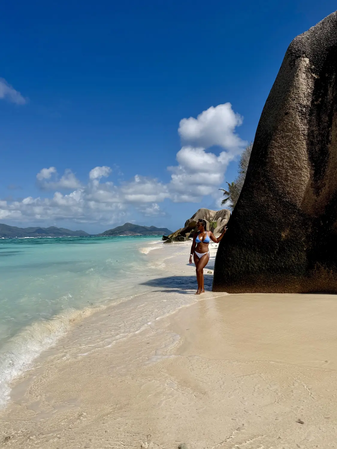 Melody leaning on a towering granite boulder at the water's edge, Anse Source d'Argent