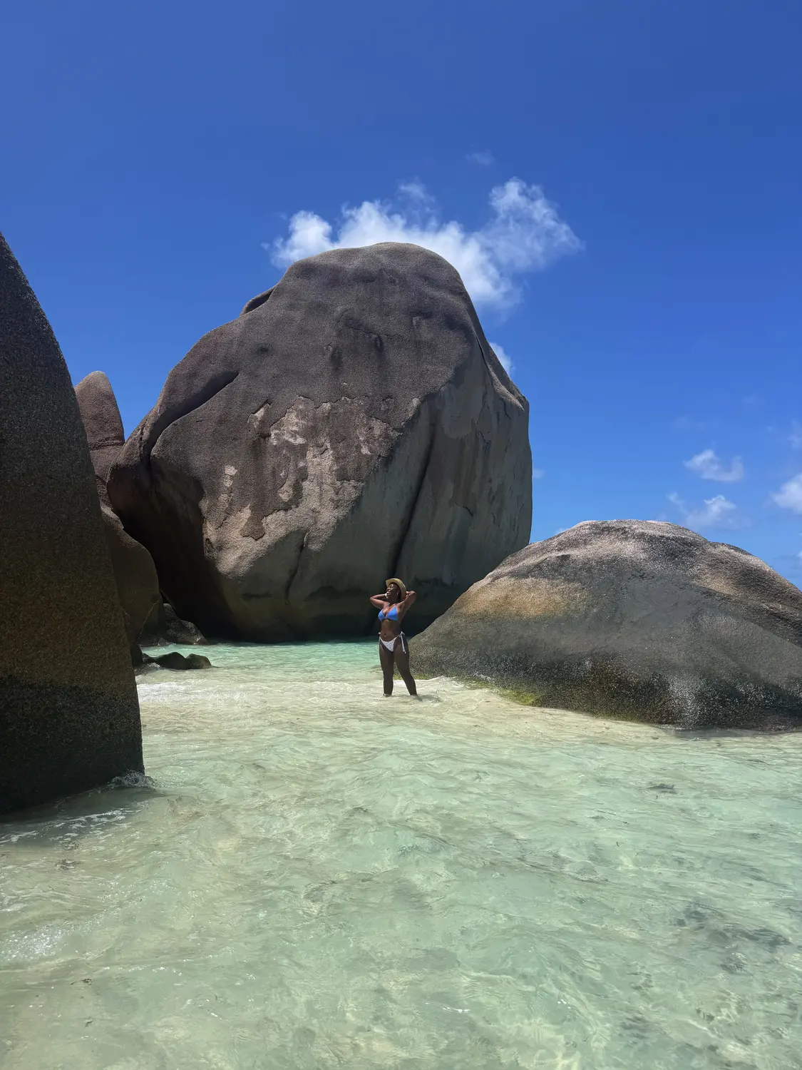 Melody standing in the clear shallows between giant granite boulders at Anse Source d'Argent