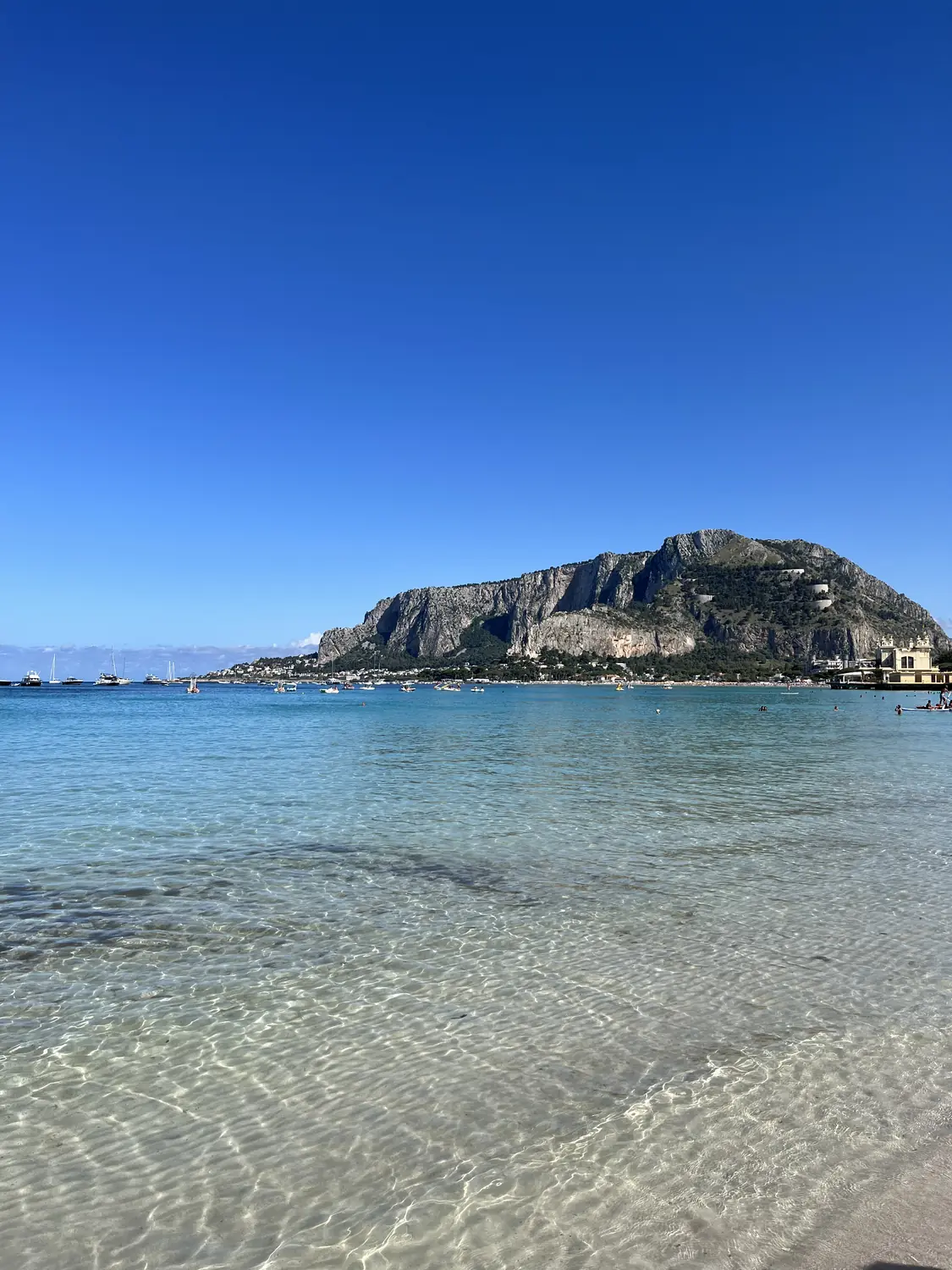 The Mondello bay and green cliffs seen across glassy clear water