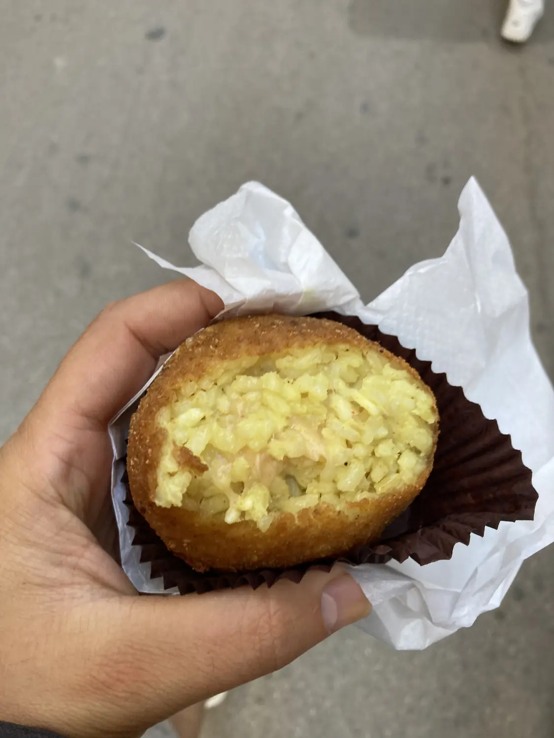 Close-up of a golden fried Sicilian arancino rice ball held in hand