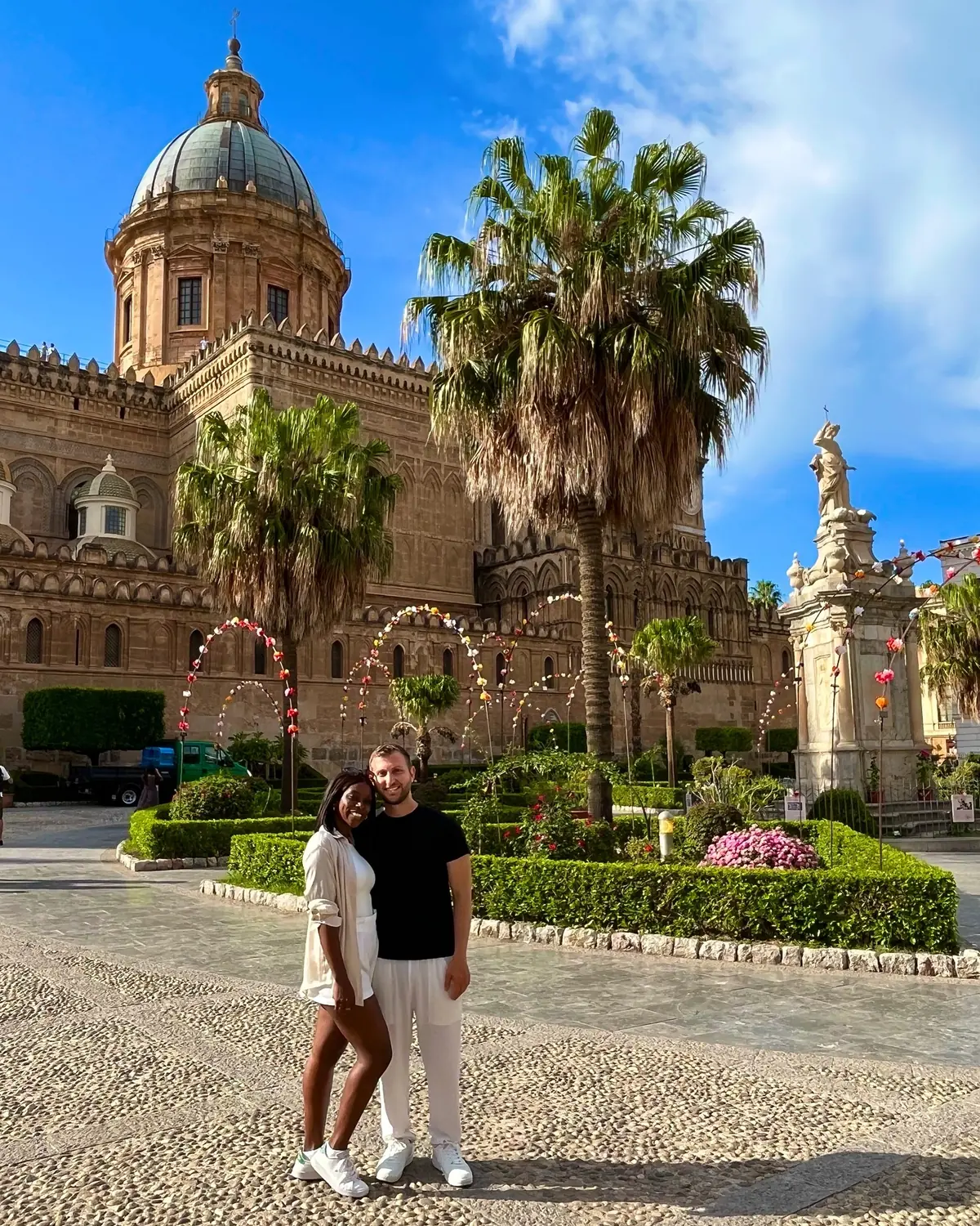 Us in front of Palermo Cathedral framed by palm trees and festival flower arches in Sicily