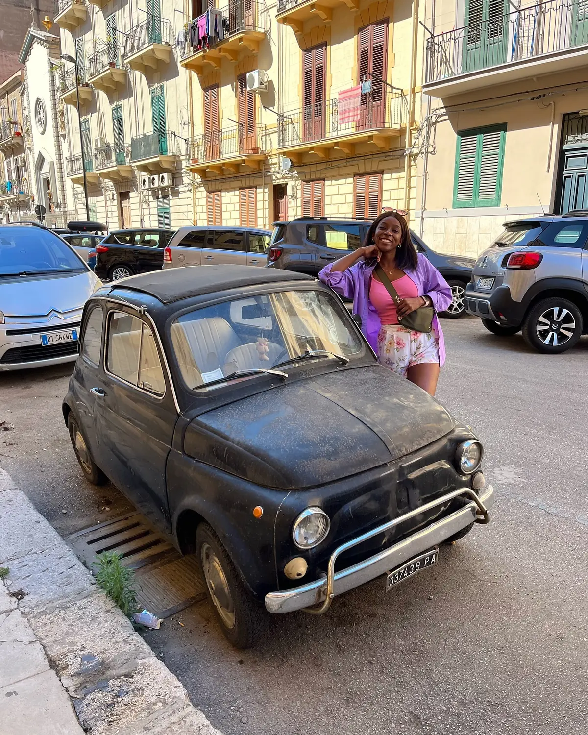 Melody leaning by a vintage black Fiat 500 on a Palermo street