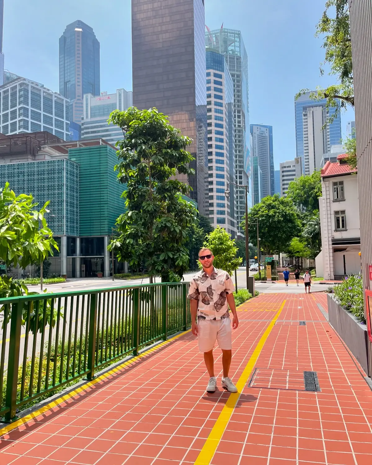 Andrew walking a tree-lined red-brick street among the Singapore skyscrapers