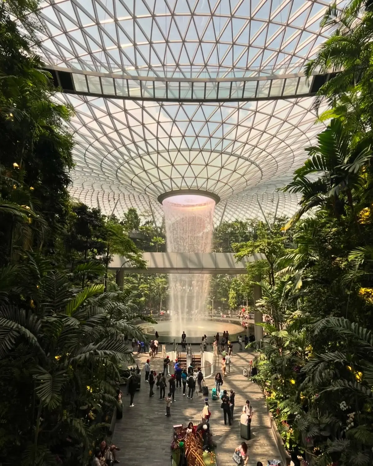 The Rain Vortex indoor waterfall pouring through the glass dome of Jewel Changi Airport surrounded by terraced forest