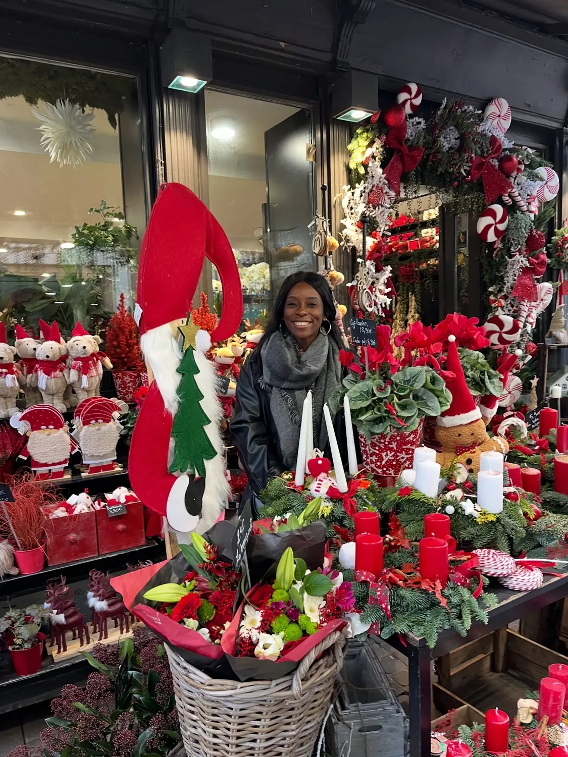 Melody smiling beside a festive florist stall packed with red Christmas decorations in Strasbourg