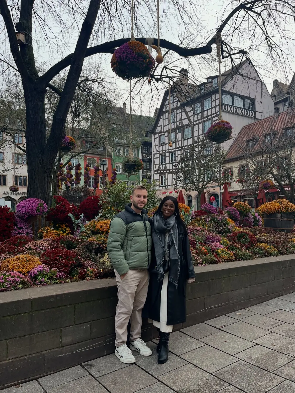 Us in front of a huge autumn-into-winter flower and pumpkin display among Strasbourg's half-timbered houses