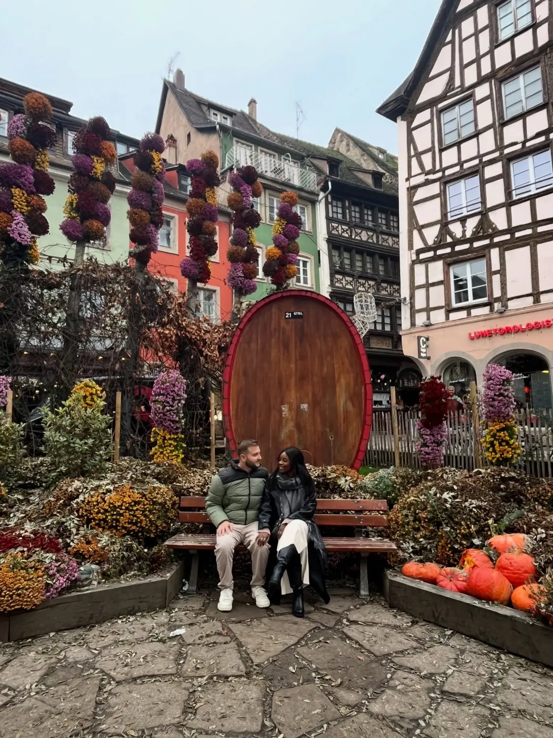 Us on a bench beside old wine barrels in Alsace, France
