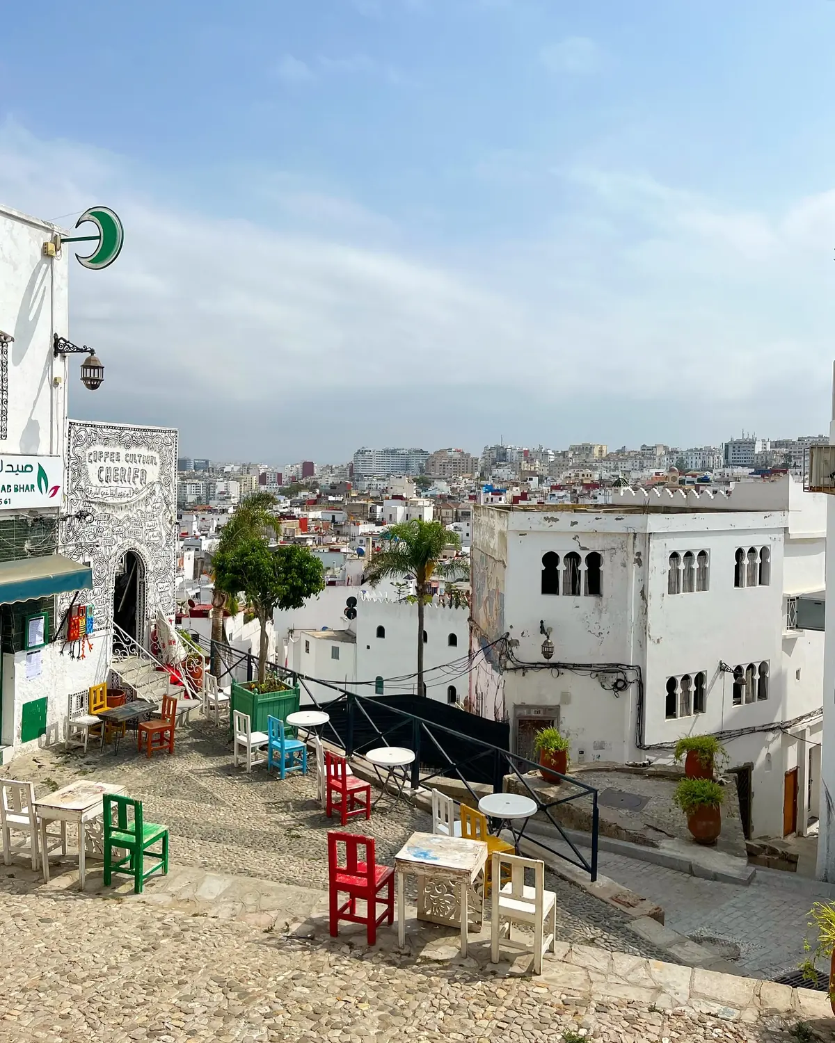 A cascade of colourful café chairs on a Tangier medina terrace above the white city and bay