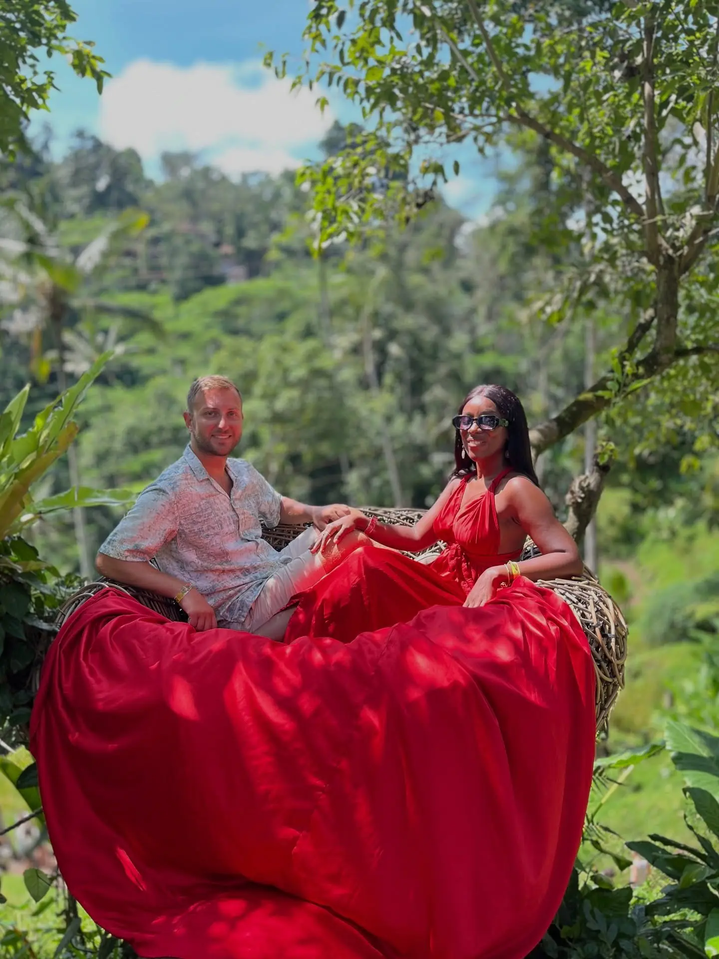 Couple in a giant nest prop with a flowing red dress over the jungle