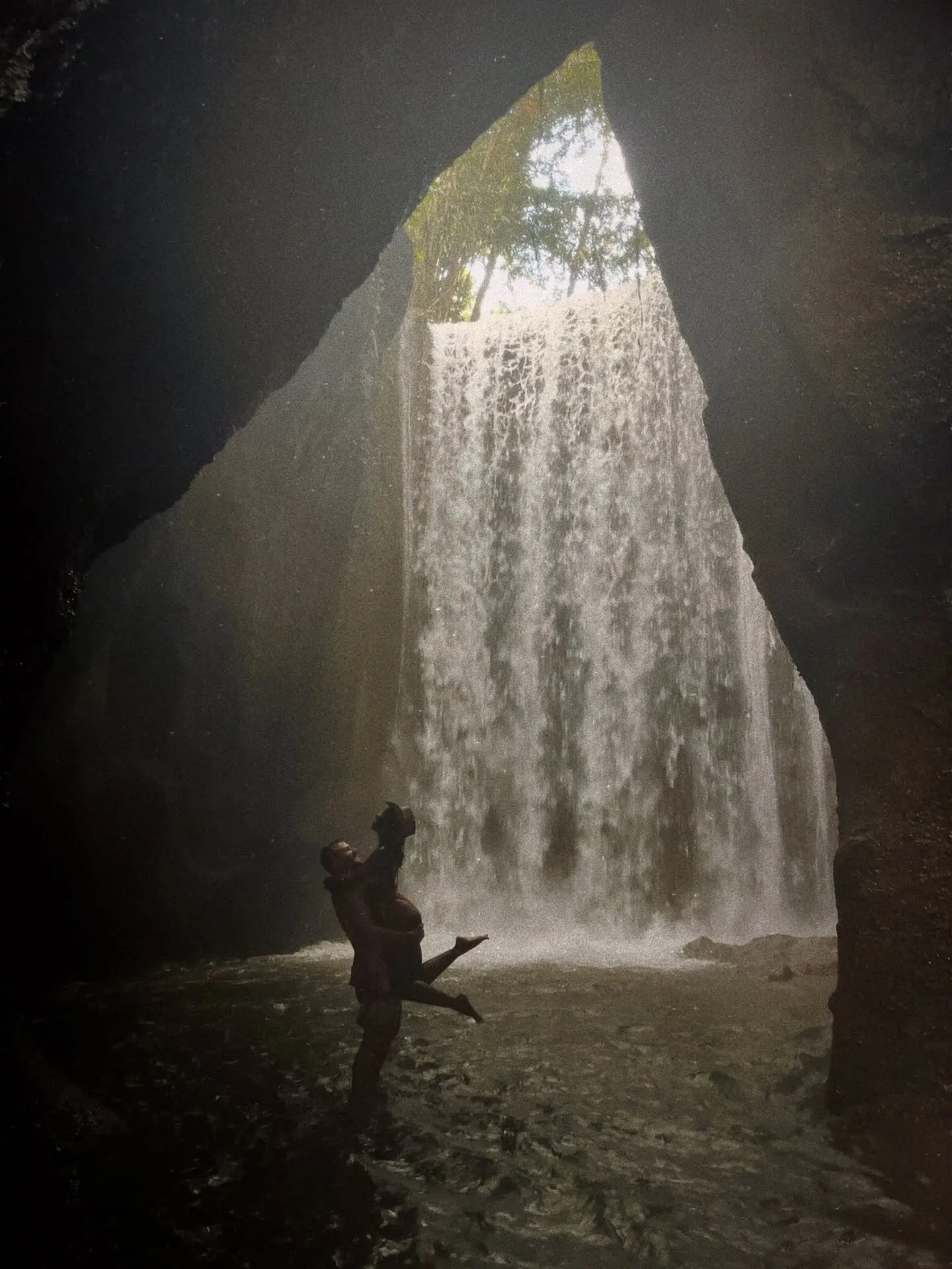 Couple beneath the light-beam waterfall inside Tukad Cepung canyon