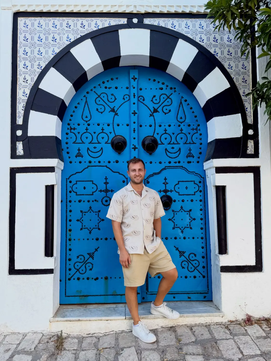 Andrew by a bright blue studded Tunisian door with a black-and-white striped arch in Sidi Bou Said