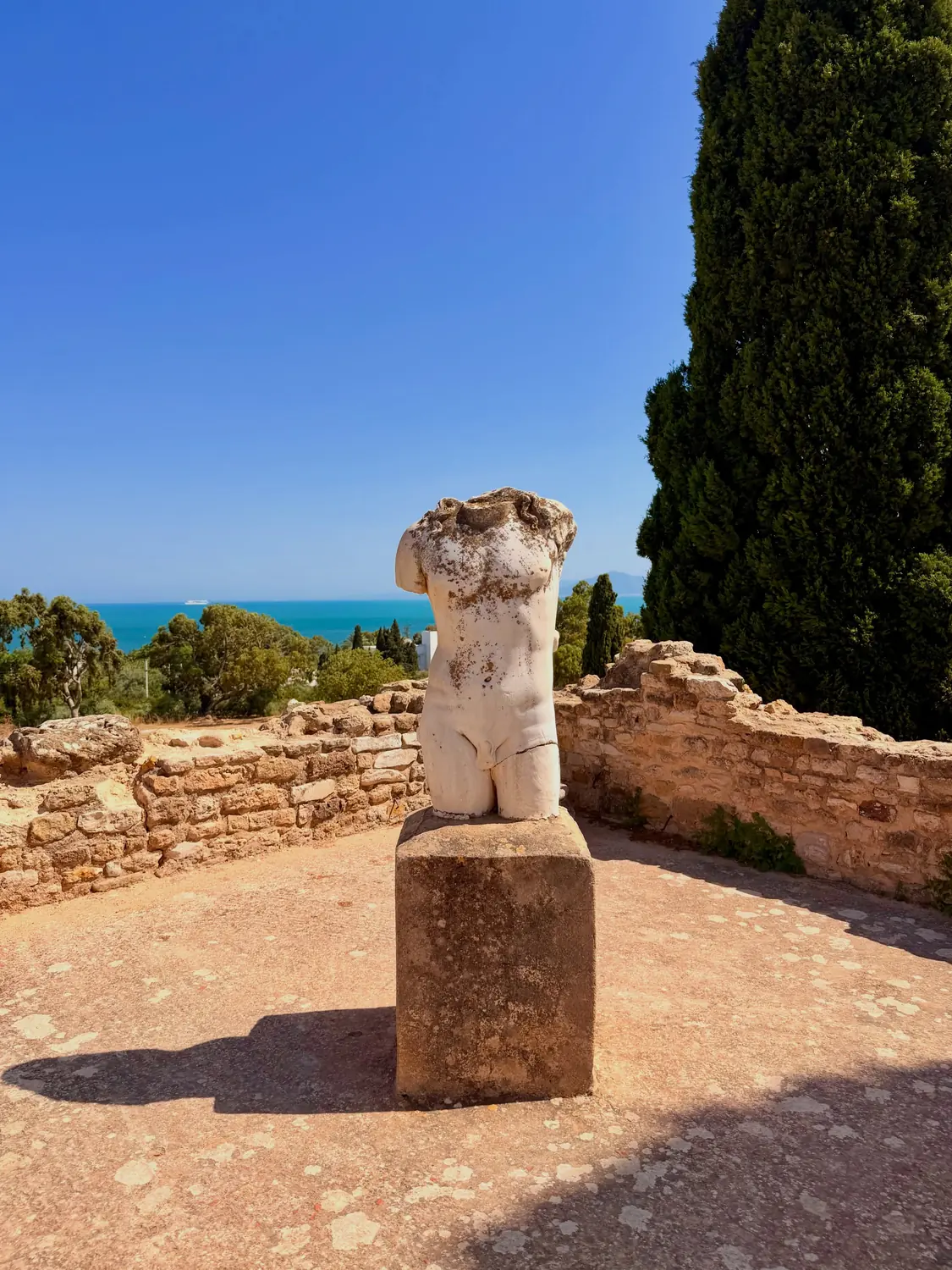 A weathered Roman marble torso on a plinth at Carthage with the sea behind