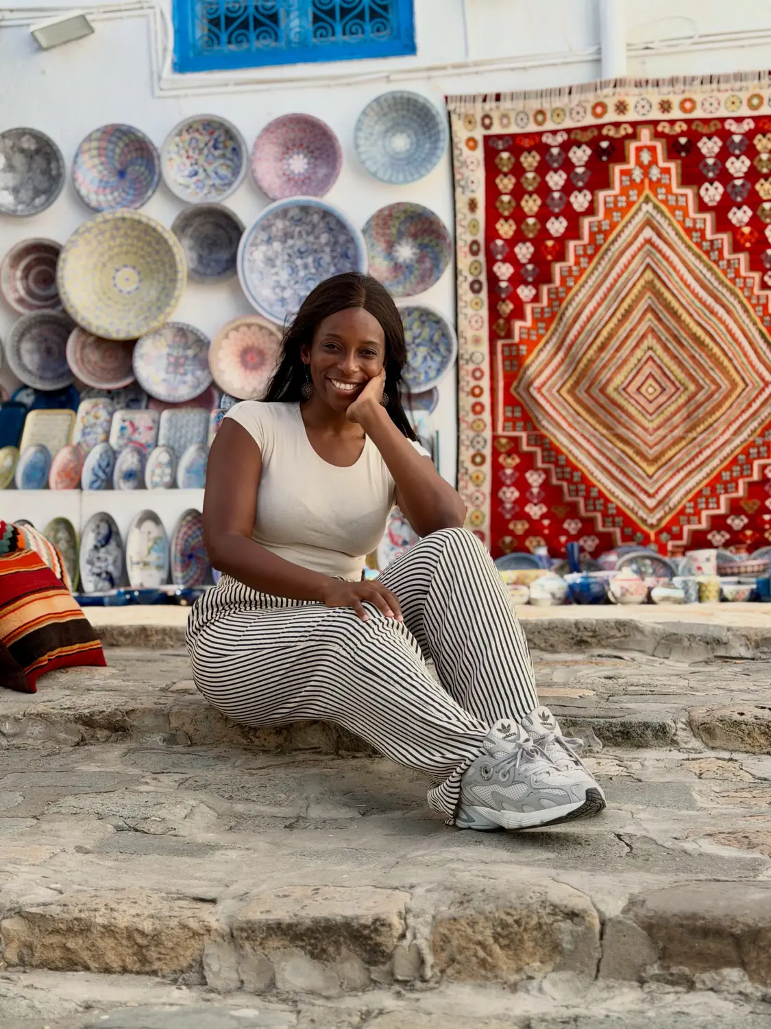 Melody sitting on steps in front of hand-painted plates and a red kilim