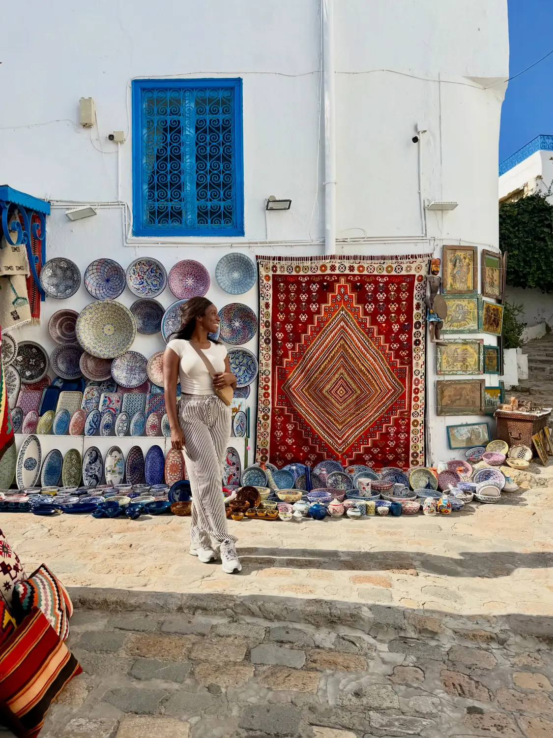 Melody walking past a wall of colourful Tunisian ceramic plates and a red carpet