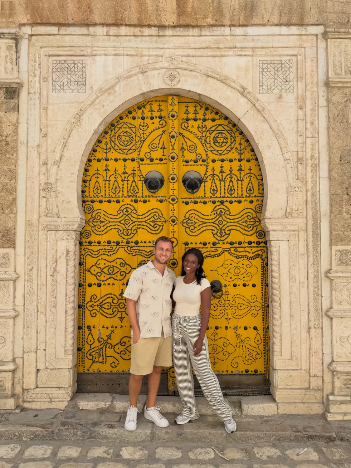 Us in front of an ornate yellow studded Tunisian door set in a carved stone arch