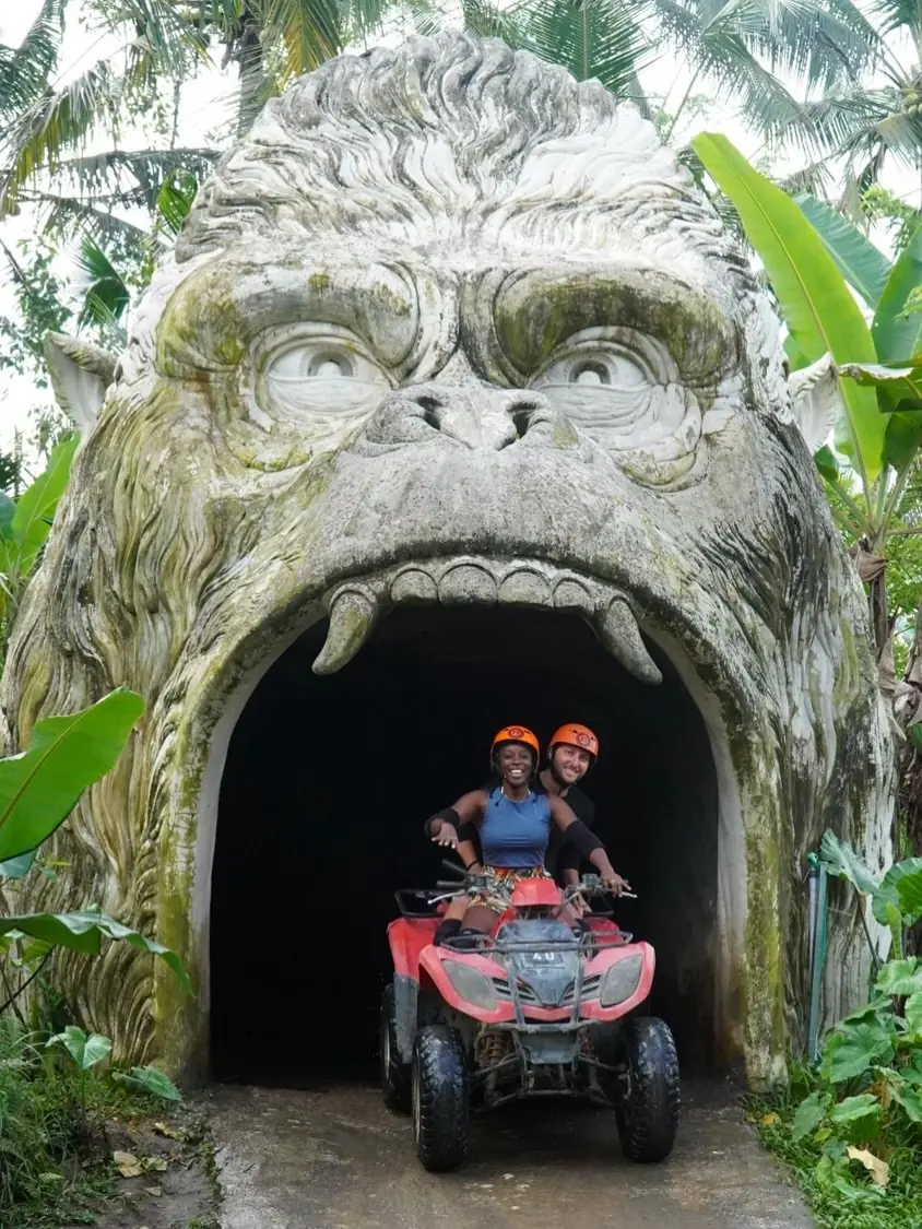 Couple riding an ATV out of a giant stone gorilla-head tunnel near Ubud