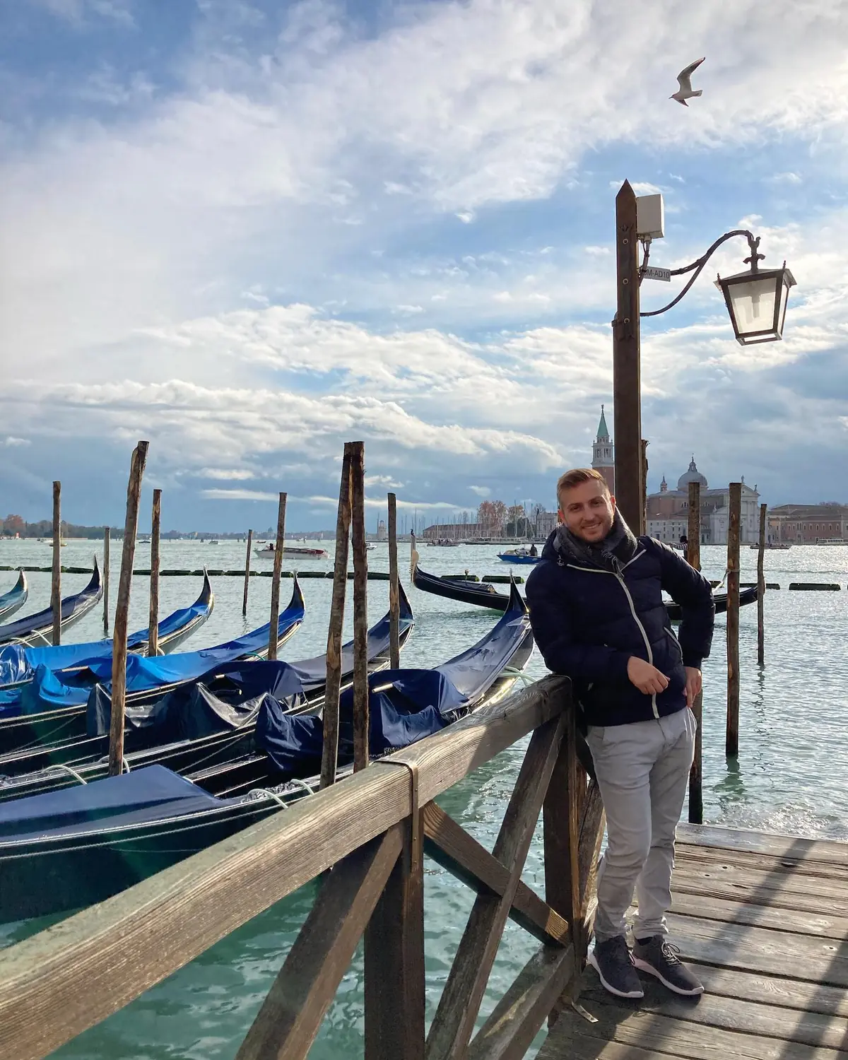 Andrew by a row of gondolas on the Venice waterfront