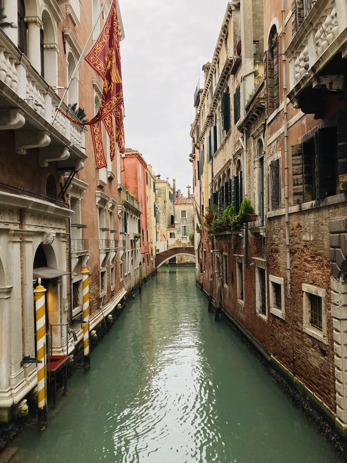 A quiet narrow canal with green water between old buildings in Venice
